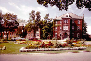 old brick institutional building with flower gardens in front