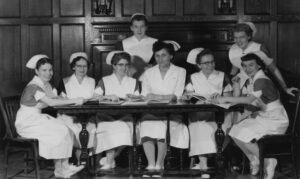 Ancienne photo en noir et blanc d’un groupe de femmes en uniforme d’infirmières souriant autour d’une table