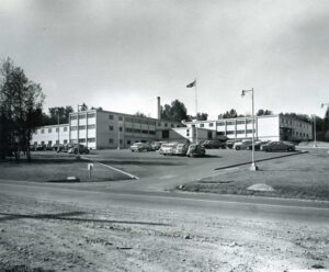 Édifice institutionnel des années 1950, à trois étages, avec des voitures stationnées devant