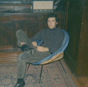 Young man with dark hair and trendy clothing sitting in chair
