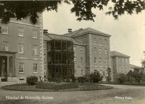 Photo en noir et blanc d'une aile d'un bâtiment institutionnel, avec une allée et un jardin devant