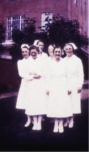 Ancienne photo en couleurs d'un groupe d'infirmières souriant devant un édifice de brique