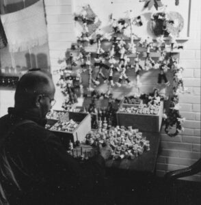 Ancienne photo en noir et blanc représentant un homme assis devant une table sur laquelle se trouvent de multiples bobines de fil