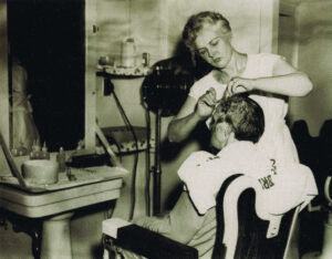 Photo ancienne d'une femme coiffant un homme dans un salon de coiffure