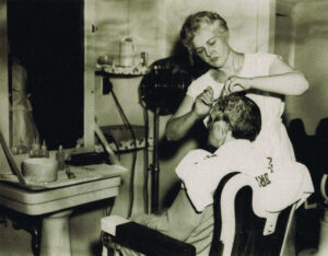 standing female hair dresser working on seated client's hair