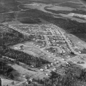 black and white aerial photograph of roads with houses and forested area