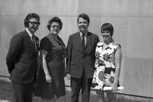 Photo en noir et blanc datant environ des années 1970 avec deux hommes et deux femmes, à l'extérieur, devant un mur de béton