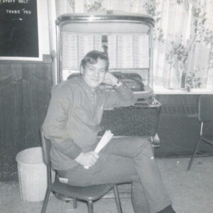 Jeune homme avec un look des anneés 1960 assis sur une chaise devant un vieux juke box