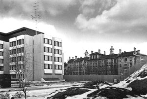 Photographie en noir et blanc des années 1970 représentant à gauche un bâtiment moderne et à droite un édifice institutionnel du 19e siècle