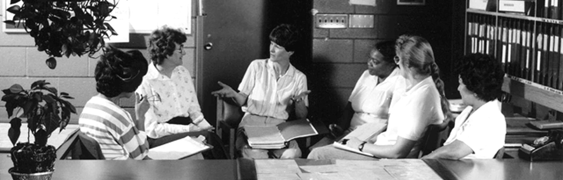 1970s black and white photograph of group of office workers or professional having a meeting or discussion in office setting