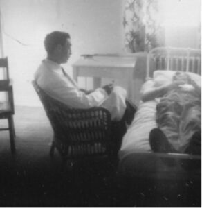 old black and white photo of man in white lab coat sitting on chair talking to patient in bed