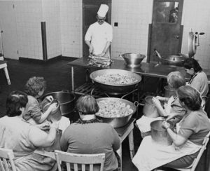 Photo en noir et blanc d'un chef cuisinier enseignant à un groupe de femmes dans une cuisine
