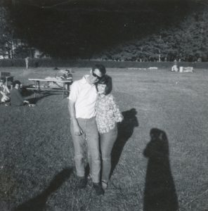 Jeune homme et jeune femme marchant dans un parc collés l'un contre l'autre, avec vêtements des années 1960