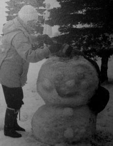 Photo en noir et blanc d'une femme décorant un bonhomme de neige