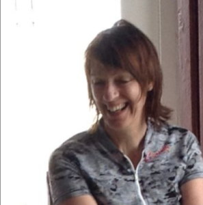 Head and shoulders shot of smiling apparent woman with dark hair, wearing cycling shirt.