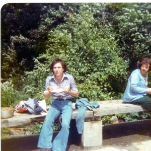two men with dark hair sitting on a wall in a park