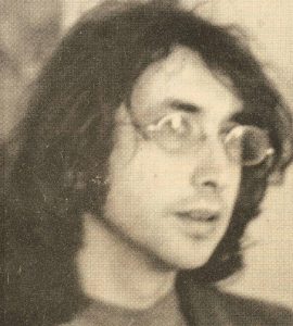 young man with long dark hair and glasses, 1970s style