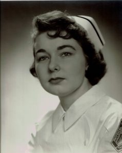 1950s graduation photo of young woman wearing white cap and nurses costume with dark hair