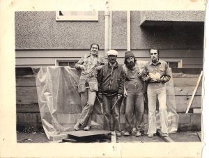 4 men standing in front of a building site wearing work clothes.