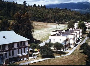 1930s and 1950s institutional buildings on wooded and grassy hillside, view of the ocean behind.