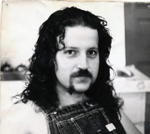 head and shoulders shot of man with thick curly dark hair and facial hair