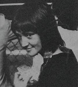 young woman with dark hair looking over her shoulder at the camera