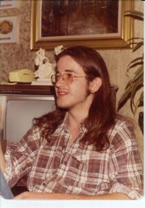 person with long brown hair sitting in front of TV wearing a plaid shirt