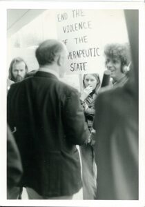 1970s protest scene, media person with headphones and mic talks to older person