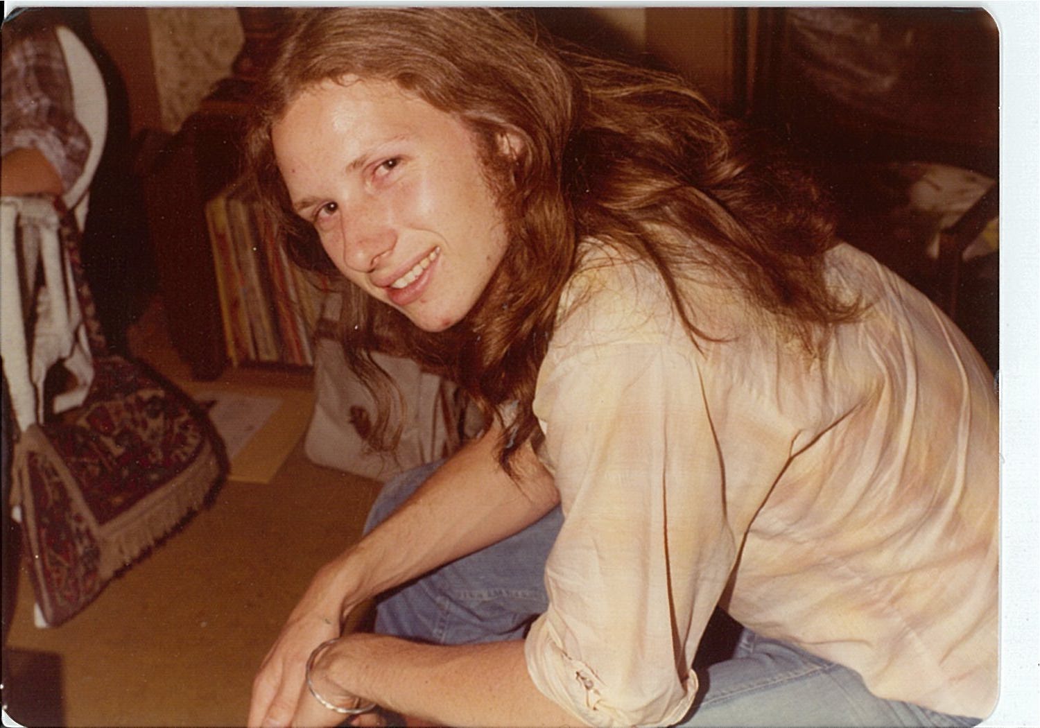 1970s person with long hair seated and turning sideways to look at the camers